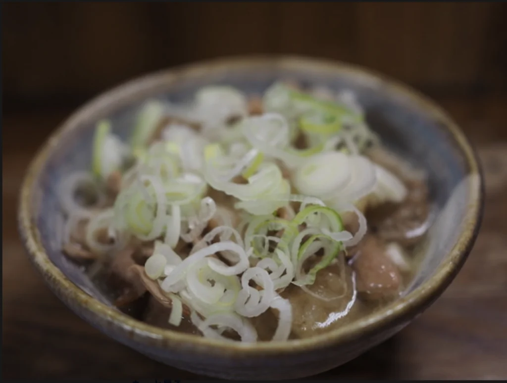 A close view of a bowl of simmered pork offal in miso broth, topped with sliced spring onion