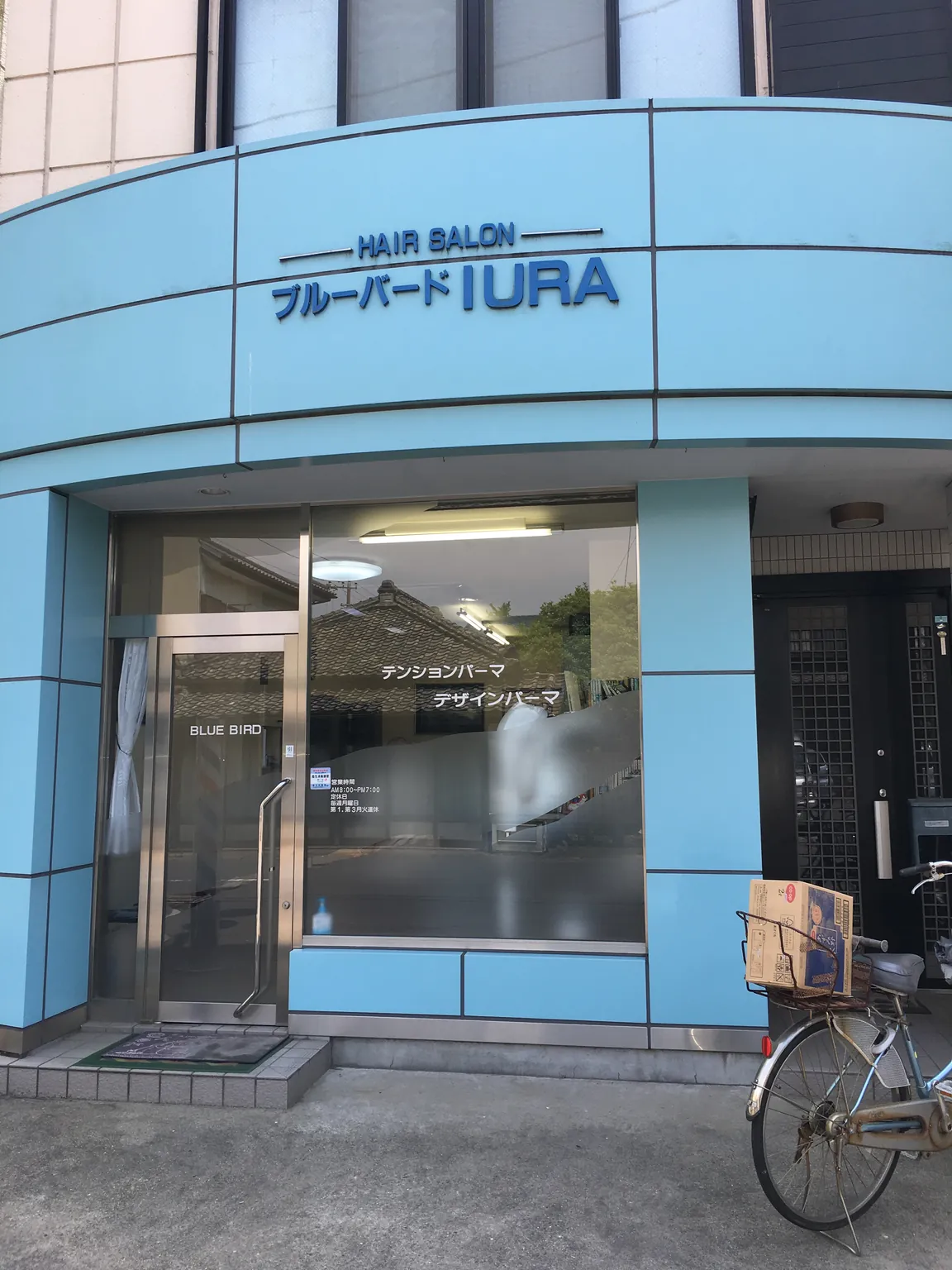 水色の外壁の理容室の店先。ガラス扉の前に自転車が一台停めてある。