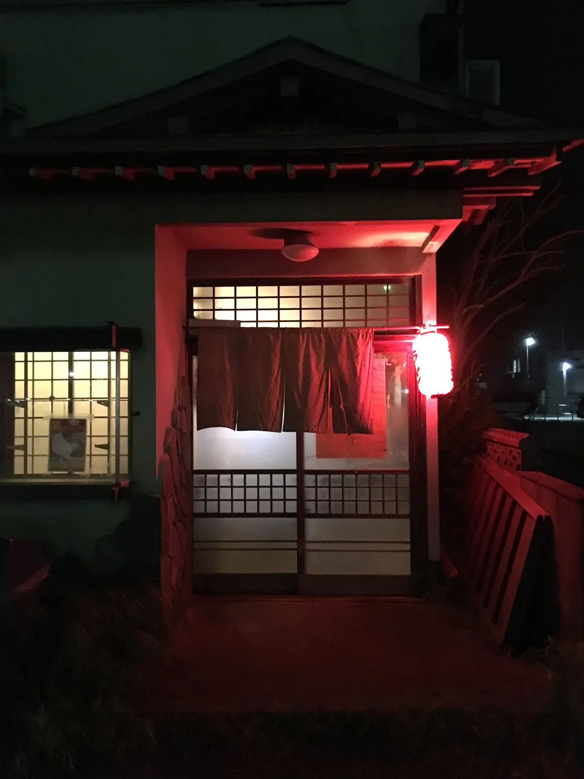 夜の「ねぎし」の入口。赤い提灯の光が引き戸と暖簾を照らしている。