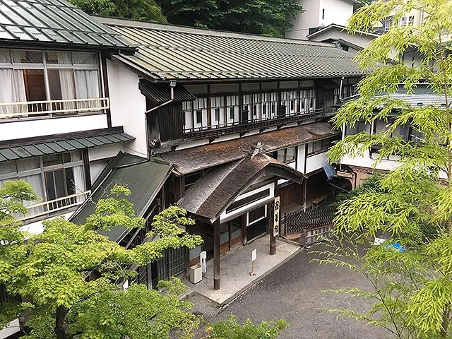 The multi-storey wooden buildings of Sekizenkan seen from above, surrounded by fresh green maples.