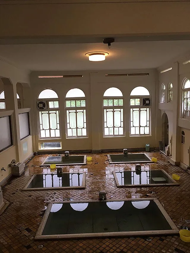 The Genroku bath: sunken stone tubs on a tiled floor beneath tall arched windows.