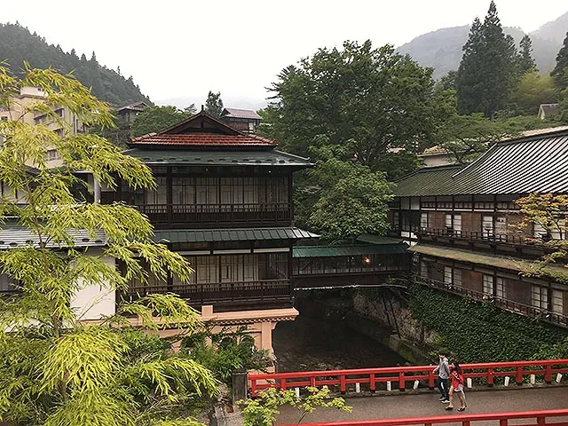 The red bridge leading to Sekizenkan's historic main building, seen between trees on a misty day.