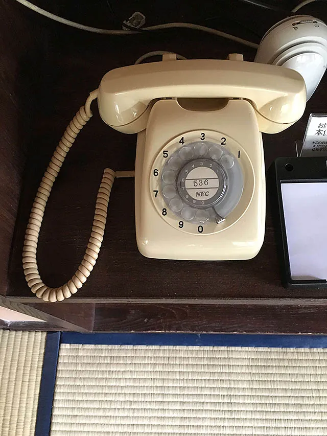 A cream-coloured rotary telephone on a dark wooden stand beside the tatami.