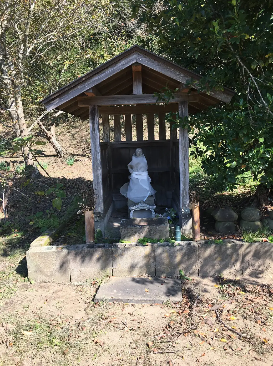 田舎道のそばに建つ小さな木の祠。中に白い石像が祀られている。