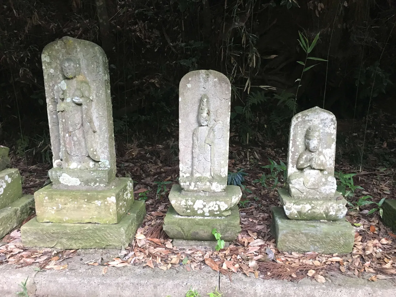 落ち葉の中、台座の上に並ぶ三体の石像。