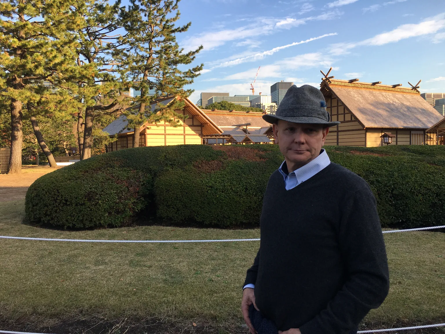 The author in a grey fedora stands before the thatched halls of the Daijōkyū.